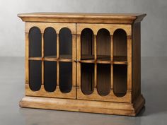 an old wooden cabinet with glass doors on the front and bottom shelves, sitting on a gray surface