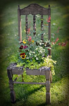 an old wooden chair with flowers growing out of it's back legs in the grass