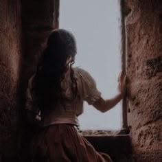 a woman is sitting in an old window sill looking out at the outside world