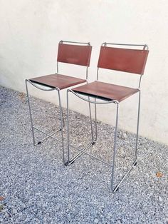 two brown chairs sitting next to each other on top of gravel covered floored ground