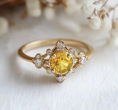 a yellow diamond ring sitting on top of a white table next to flowers and branches