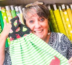 a woman is holding up some cloths in front of a shelf full of colorful fabrics