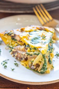 a slice of quiche with spinach and cheese on a plate next to a fork