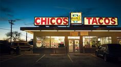 a taco shop at night with cars parked in the parking lot and lights on