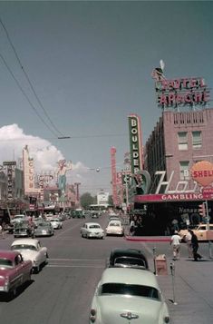 an old photo of cars driving down the street in front of neon signs and buildings