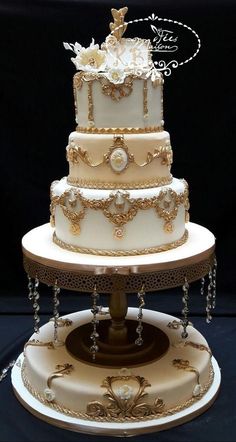 a three tiered wedding cake with white and gold decorations on the top, sitting on a stand