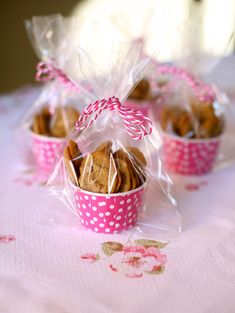 three pink polka dot cups filled with cookies on top of a white cloth covered table