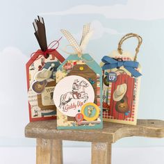 three gift bags sitting on top of a wooden bench with tags attached to the handles