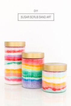 three jars filled with colorful sugar scrubs sitting on top of a white table next to each other