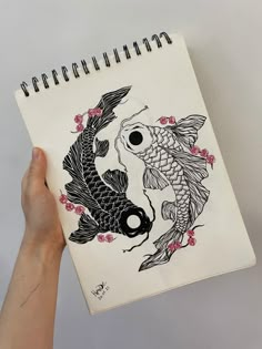 a hand holding a notebook with a drawing of two koi fish