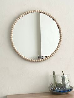 a round mirror mounted on the wall above a table with a vase and cactus in it