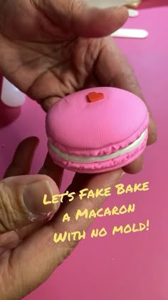 a pink macaron with a red heart on it being held by someone's hand