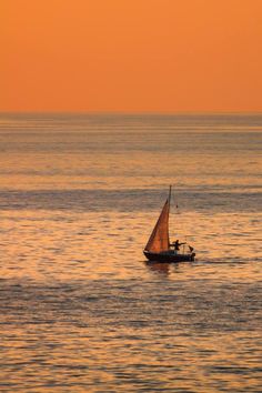 a small sailboat in the middle of an ocean at sunset, with one person on it's back