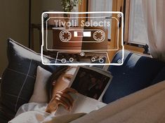 a woman reading a book while sitting on a couch with a cassette player above her head