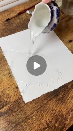 someone pouring water into a cup on top of a piece of paper that is sitting on a table