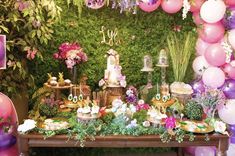 a table topped with lots of pink and purple balloons next to a lush green wall