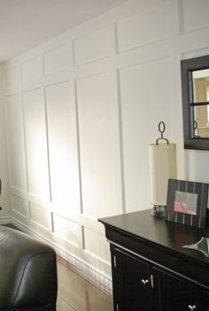 a living room with white paneling and black leather chair in the corner, next to a dresser