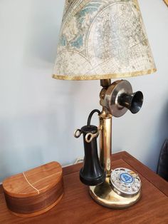 an old fashioned telephone sitting on top of a wooden table next to a lamp shade