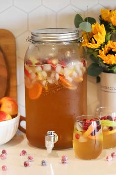 the pitcher is full of water and has fruit in it, along with two glasses