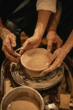 two people are making pottery on a potter's wheel, with their hands touching the bowl