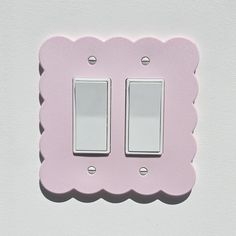 a pink light switch cover with scalloped edges on a white wall in the daytime