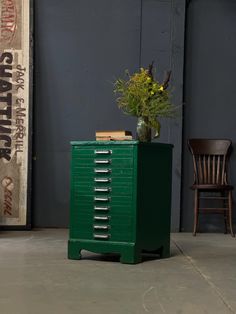 a green filing cabinet sitting next to a wooden chair with a flower pot on top