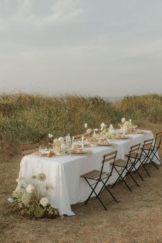 a table set up with white flowers and place settings for an outdoor dinner in the grass