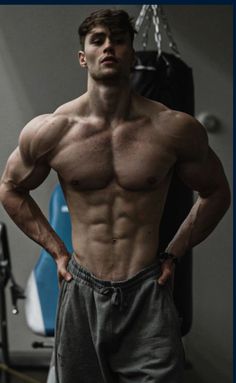 a shirtless man standing in front of a gym machine with his hands on his hips