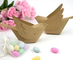 two paper doves sitting next to candy candies on a white surface with pink flowers in the background