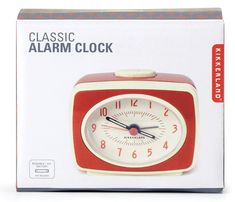 an alarm clock in the shape of a red square with white face and hands, sitting on top of a box