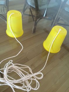 two yellow plastic cups sitting on top of a wooden floor next to a chair and table