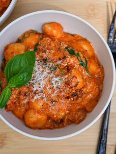 a white bowl filled with pasta and sauce on top of a wooden table next to silverware