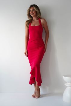 a woman in a red dress leaning against a wall