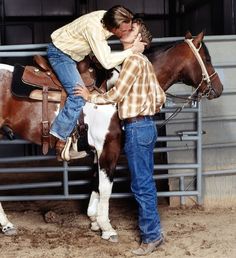 a man kissing a woman on the cheek while standing next to a brown and white horse