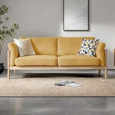 a living room with a yellow couch and two planters on the floor, in front of a gray wall