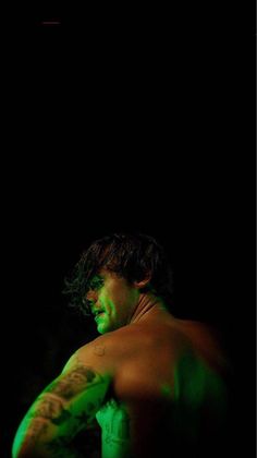 a shirtless man with green paint on his face and chest, standing in the dark