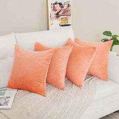 four orange pillows on a white couch in a living room with a potted plant