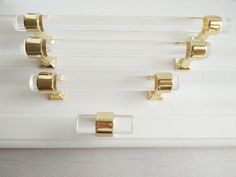 four gold - plated hooks hang on a white glass shelf with clear acrylic