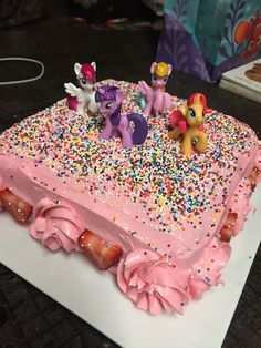 a cake with pink frosting and sprinkles has pony figures on it