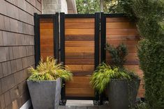 two large planters sitting next to each other in front of a wooden fenced entrance