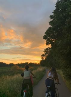 two people riding bikes down a path at sunset or dawn with trees in the background