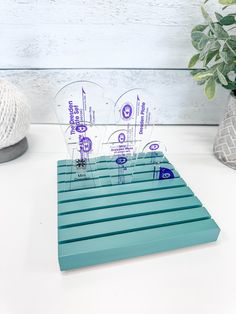 four clear acrylic business cards sitting on top of a blue plastic shelf next to a potted plant