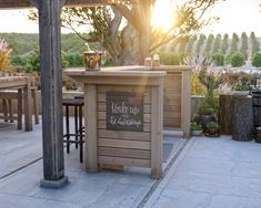 an outdoor bar with wooden tables and stools under a tree in the evening sun