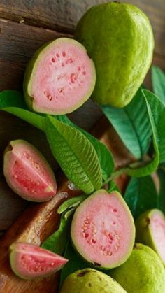 some green and pink fruit sitting on top of a wooden cutting board next to leaves