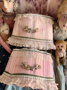 three dolls sitting next to each other on top of a bed with pink sheets and ruffled bedspread