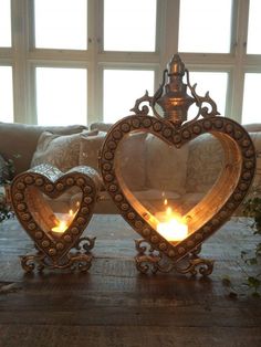 two heart shaped candles sitting on top of a wooden table in front of a window