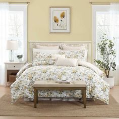 a bedroom with yellow walls and white curtains on the windowsills is decorated in floral bedding