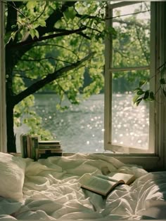 an open book sitting on top of a bed in front of a window next to a tree