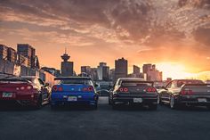 four cars are parked in front of a cityscape with the sun setting behind them