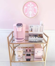 a pink and gold starbucks coffee station with various items on it in front of a wall